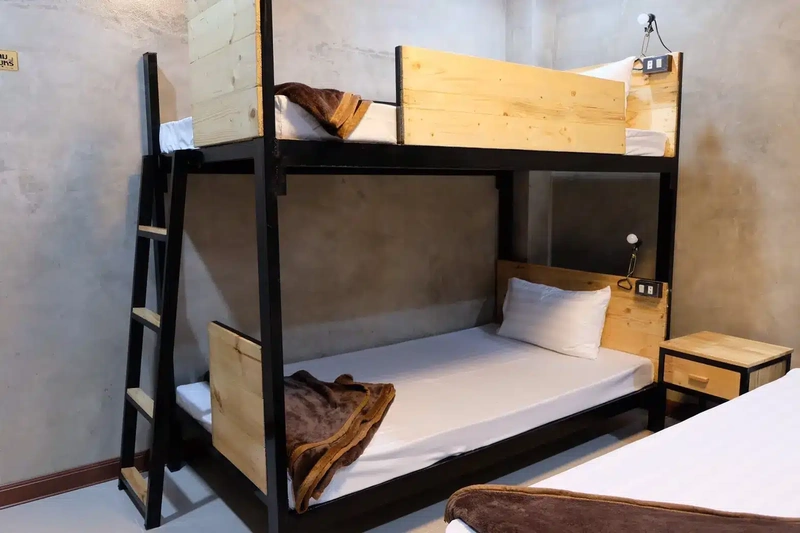 A dormitory room with a bunk bed and a single bed made up in white