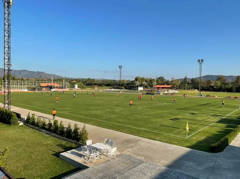 The pitch seen from the raised terrace, a floodlight tower and mountains behind