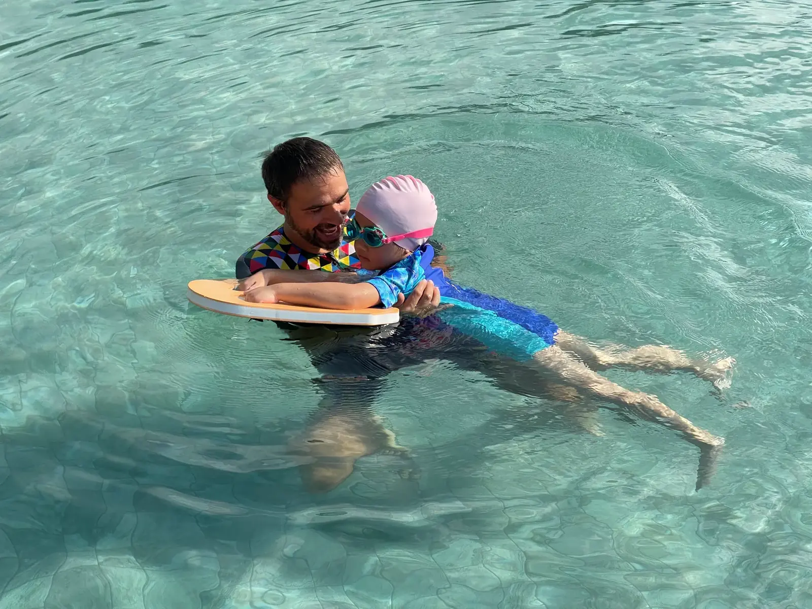 A swimming coach supporting a child on a float in the pool