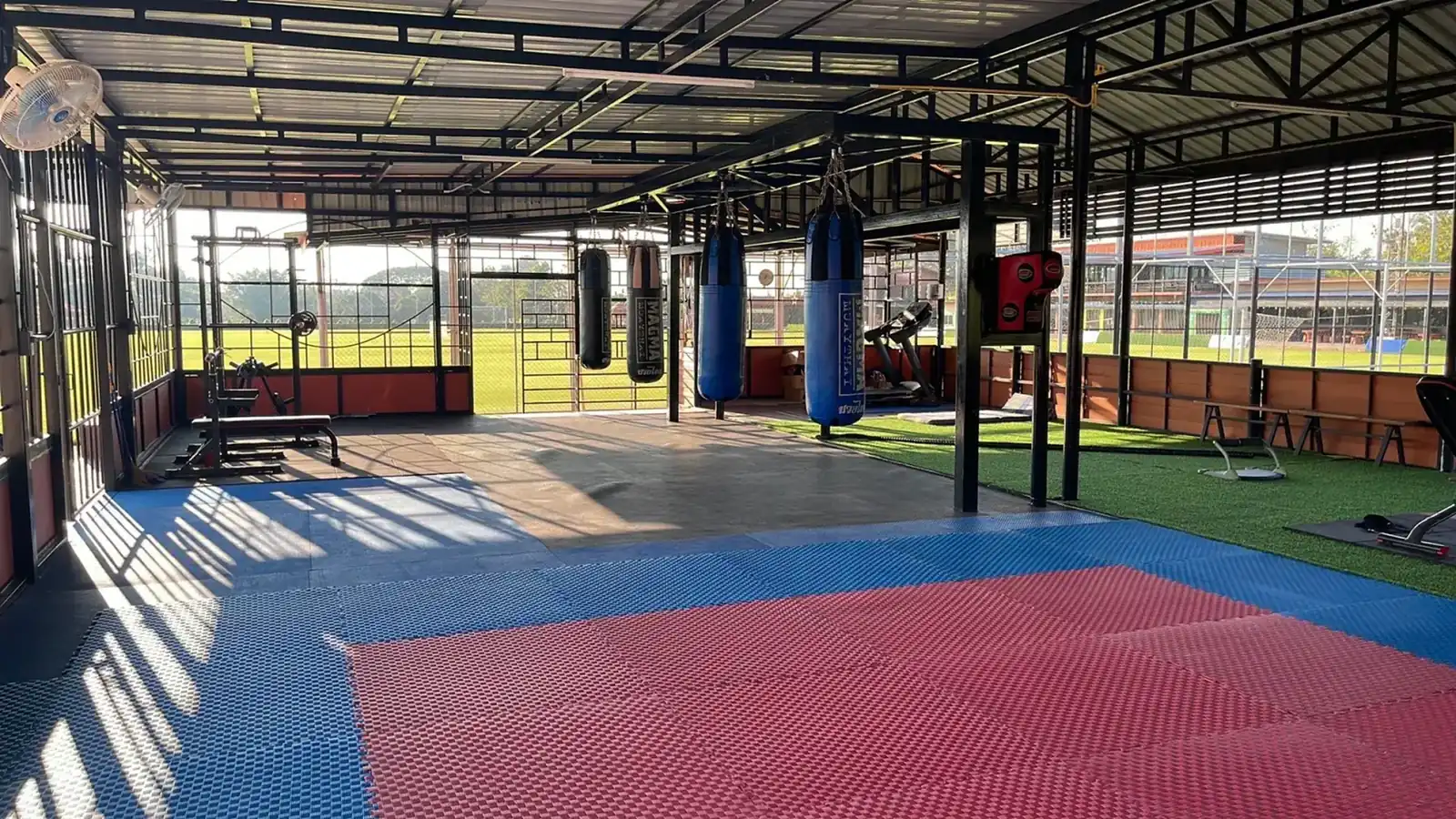 Open-sided training hall with punch bags, mats and gym equipment beside the pitch